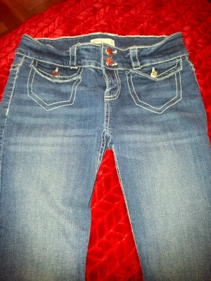 Blå jeans med kontrastsömmar - Snygga blå jeans med vita kontrastsömmar och dubbla knappar i midjan. Jeansen har klassiska fem fickor och dekorativa sömmar på bakfickorna. Materialet är denim med lätt tvättad look och raka ben.