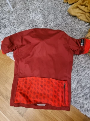 Röd cykeltröja från Bontrager - Snygg röd cykeltröja från Bontrager med kort ärm och dragkedjeficka bak. Nederdelen har ett mönstrat parti i rött och svart. Perfekt för cykelturer och träning. Tröjan är tillverkad i ett lätt och funktionellt material som andas.