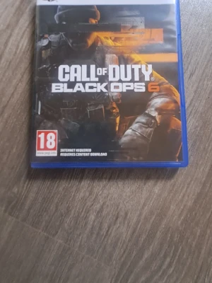 Nyt Call of Duty Black Ops 6 PS5 - Call of Duty Black Ops 6 till PlayStation 5. Omslaget är svart och blått med en soldat i fokus och orange detaljer. Spelet är ett actionfyllt FPS med multiplayer och zombies-läge. Rekommenderas från 18 år. Fodralet är av plast.
