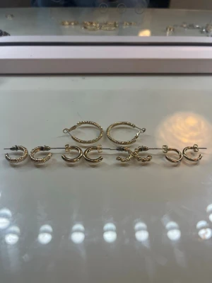 Set med sex par guldiga örhängen - Säljer ett set med sex par små guldiga örhängen i olika former, bland annat tvinnade och släta hoops. Alla är i metall med glansig finish och passar perfekt för att mixa och matcha. Märke saknas.