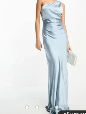 Ljusblå one-shoulder balklänning  - Elegant ljusblå långklänning i glansigt satinmaterial med oneshoulder-design. Klänningen har en figurnära passform och vackra draperingar över midjan. Perfekt för dig som vill sticka ut på bal eller fest. Sedan så finns det däremot en liten tråd längst ner på klänningen som har dragit sig lite men det märks inte av. 