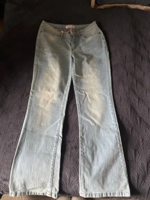 Ljusblå bootcut jeans - Säljer ett par ljusblå bootcut jeans med klassisk femficksdesign och låg midja. Jeansen har en avslappnad passform och är tillverkade i denim. Perfekta för en casual look.