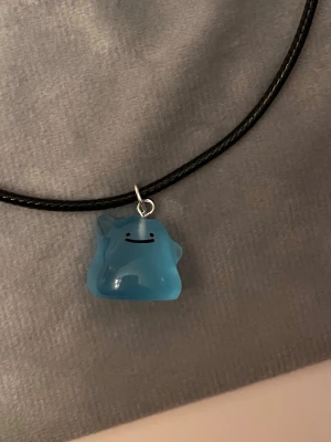 Självlysande Shiny Ditto halsband Pokémon smycke  - Så gulligt halsband med en berlock av en shiny Ditto!Berlocken är ca 1,5 x 1,5 cm och trädd på svart tråd. Den är också självlysande och lyser i mörkret. Halsbandet är justerbart 40-45 cm. 