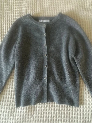 Grå kofta med pärlknappar från Zara - Supersnygg grå stickad kofta från Zara med silvriga pärlknappar. Koftan har rund halsringning och långa ärmar. Typ aldrig använd så jättebra skick! Storlek S men den är lite liten i storleken! 