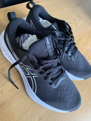 Svarta Asics sneakers med vit sula - Svarta sneakers från Asics med klassisk vit sula och vita detaljer på sidorna. Ovandelen är i meshmaterial för bra andningsförmåga och skon har svarta skosnören. Perfekt för dig som gillar sportig och stilren look.