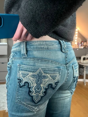 Blå jeans med broderade bakfickor - Snygga ljusblå jeans med coola broderier på bakfickorna. Jeansen har klassisk femficksdesign, låg midja och raka ben. Materialet är slitstarkt denim och detaljerna på fickorna ger ett unikt uttryck. Perfekta för dig som vill sticka ut lite extra.(Är 170cm står ingen storlek men ungefär xs-s)
