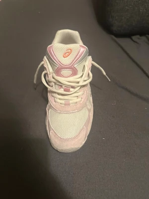 Vita och rosa Asics sneakers - Snygga sneakers från Asics i vitt och ljusrosa med mesh och syntetdetaljer. Skorna har klassisk snörning och låg profil, perfekt för en sportig och trendig look. Asics-logga i orange på plösen och hälen. Kan sänka priset vid snabb försäljning 