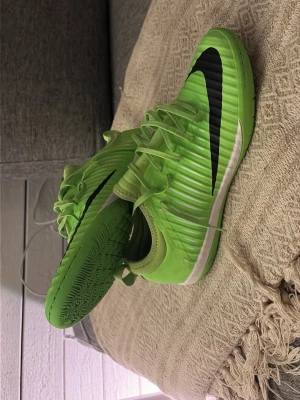 Nike gröna fotbollsskor med svart swoosh - Säljer ett par grymma gröna fotbollsskor från Nike med svart swoosh och vita detaljer. Skorna har snörning, räfflad ovansida och slitstark sula för bra grepp på planen. Perfekta för dig som vill sticka ut på matchen eller träningen.