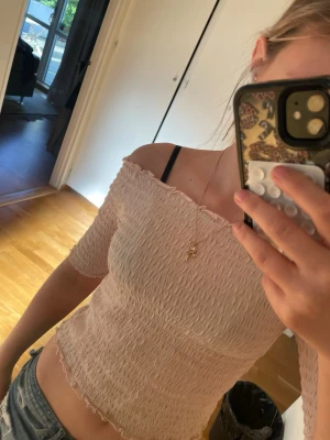 Ljusrosa offshoulder topp - Söt ljusrosa offshoulder topp med smockad struktur och croppad passform. Toppen har korta ärmar och volangkant upptill och nedtill. Perfekt för varma dagar och en trendig look.