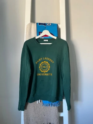  Saint Laurent crewneck/sweatshirt - Mörkgrön crewneck från Saint Laurent med gult universitetsinspirerat tryck på bröstet. Hör av dig vid frågor eller bud.