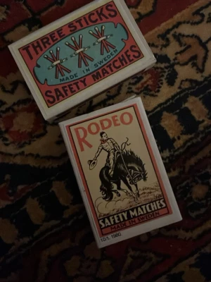 Samlaraskar med tändsticksetiketter - Två samlaraskar med klassiska svenska tändsticksetiketter: 'Three Sticks' och 'Rodeo'. Båda askarna är tillverkade i Sverige och har färgglada, retroinspirerade motiv. Baksidan visar info om jubileumsserier och gamla etiketter. Perfekt för samlare av nostalgi och svensk design.
