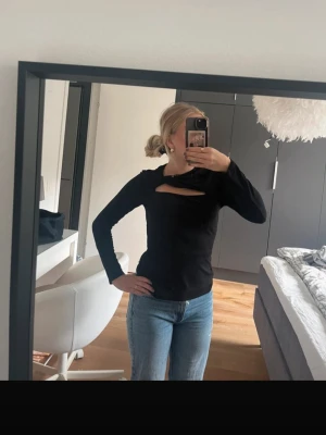 Svart långärmad topp med cut out - Trendig svart långärmad topp med en snygg cut out-detalj vid bröstet. Modellen är figurnära och toppen har en enkel, stilren design som passar till mycket. Perfekt för dig som vill ha något lite extra till din outfit.