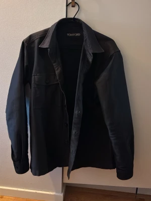 Svart overshirt från Tom Ford - Overshirt i svart från Tom Ford med klassisk krage, knappstängning och en bröstficka. Sjukt bra kvalitet, använd några få gånger men fortfarande i väldigt bra skick.