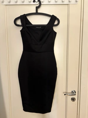Svart figurnära klänning Boohoo - Snygg svart klänning från Boohoo med figurnära passform och breda axelband. Klänningen har en djup v-ringning och är knälång, perfekt för en trendig look. Materialet är slätt och stretchigt för en bekväm känsla.