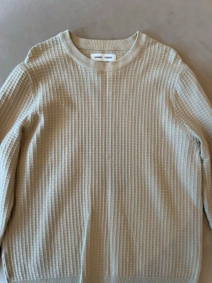 Beige strukturerad tröja från Samsoe Samsoe - Säljer en beige långärmad tröja från Samsoe Samsoe med snyggt rutmönstrad struktur. Tröjan har rund halsringning och ribbade muddar vid ärmslut och nederkant. Perfekt för en stilren och avslappnad look.