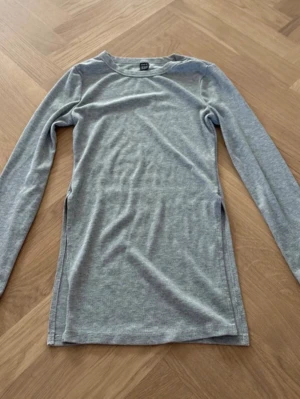 Grå långärmad topp i bomull - En enkel och stilren grå långärmad topp i mjuk bomull. Modellen är rak med rund halsringning och passar perfekt till jeans eller kjol. Tidlös design som är lätt att matcha med andra plagg.