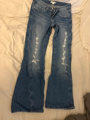 Blå bootcut jeans från Gina - Snygga blå bootcut jeans från Sweetheart med slitna detaljer framtill och dekorativa sömmar på bakfickorna. Jeansen har klassisk femficksmodell och är tillverkade i denim med en cool vintagekänsla. Perfekta för en avslappnad och trendig look.