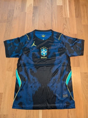 Brasilien matchtröja Nike x Jordan. Storlek.S.M. - Helt ny, Snygg Brasilien matchtröja från Nike x Jordan med svart och blått mönster, gula detaljer och CBF-logga på bröstet.       Finns S.ML storlek.Tillverkad i lätt och ventilerande material, perfekt för fotboll eller träning. Rund hals och korta ärmar för maximal rörelsefrihet.