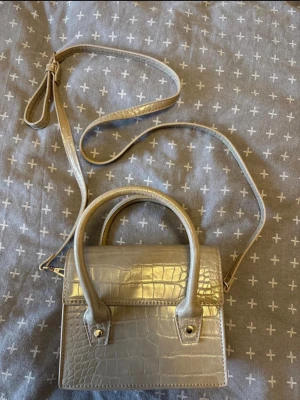 Beige miniväska med krokoprägling - Snygg beige handväska i ministorlek med krokodilpräglat mönster. Väskan har både handtag och en lång axelrem som går att justera. Stilren och trendig fyrkantig form, perfekt för att lyfta din outfit.