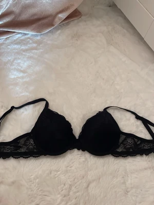 Svart push-up bh med spetsdetaljer - Säljer en svart push-up bh med vadderade kupor och fina spetsdetaljer på sidorna. Axelbanden är justerbara och bh:n har en klassisk hakknäppning bak. Har spets som ger en elegant look.