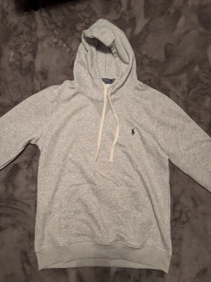 Grå hoodie från Polo Ralph Lauren -  hoodie från Polo Ralph Lauren med klassisk huva och vita dragsnören. I Storlek M/L