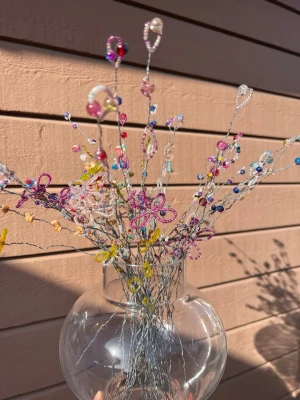 Färgglada pärlblommor  - Unika handgjorda blommor av metalltråd och pärlor i olika färger som rosa, blå, gul och lila. Blommorna är arrangerade i en rund, genomskinlig glasvas. Perfekt som dekoration för att ge rummet en kreativ och lekfull touch. (Vasen ingår inte) 