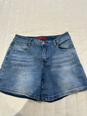Blå jeansshorts med fem fickor - Snygga blå jeansshorts med klassisk femficksdesign och bälteshällor. Shortsen har knapp- och dragkedjestängning framtill och är tillverkade i ett slitstarkt denimtyg. Perfekta för varma dagar och enkel att matcha med olika toppar.