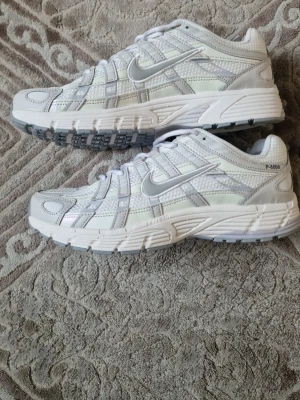 Nike P-6000 vita sneakers - Nike P-6000 sneakers i vitt och silver med mesh och syntetiska överdrag. Skorna har en chunky sula och tydliga detaljer längs sidorna samt Nike-logga på både sidan och sulan. Perfekta för en sportig och trendig look.