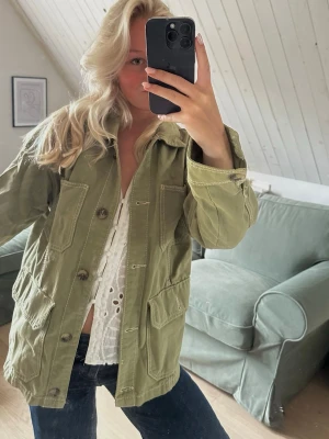 Olivgrön jeansjacka - Snygg olivgrön jeansjacka med stora framfickor och knappar framtill. Jackan har en avslappnad passform och är perfekt att slänga över en t-shirt eller topp. Enkel, stilren och lätt att matcha.