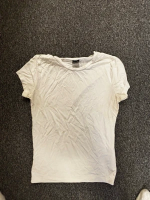 Vit basic t-shirt från Gina Tricot - En enkel vit t-shirt från Gina Tricot i storlek M. T-shirten har rund halsringning och korta ärmar, perfekt som basplagg till alla outfits. Tillverkad i mjukt material för en bekväm känsla.