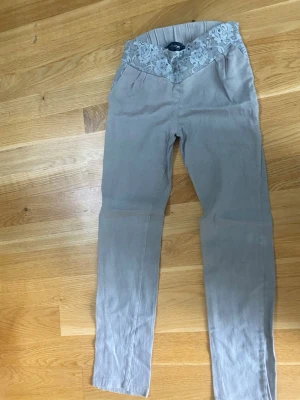 Beiga manchesterbyxor med spetsdetalj - Snygga beiga manchesterbyxor från Fashion med hög midja och unik spetsdetalj med blommönster och små pärlor i midjan. Byxorna har smal passform och är perfekta för dig som vill ha något extra i garderoben.