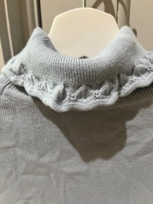 Ljusblå ribbad polotopp med volang - Supersöt ljusblå ribbad polotopp med volangdetaljer i kragen, ärmslut och nederkant. Toppen har korta ärmar och är gjord i ett mjukt, stretchigt material som sitter snyggt på kroppen. Perfekt för dig som gillar en feminin och trendig stil.