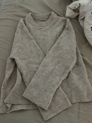 Beige stickad tröja från Gina Tricot - Mysig beige stickad tröja från Gina Tricot i premiumkvalitet. Tröjan har rund halsringning, långa ärmar och ribbade muddar vid ärmslut och nederkant. Perfekt för lager-på-lager och enkel att matcha med jeans eller kjol.