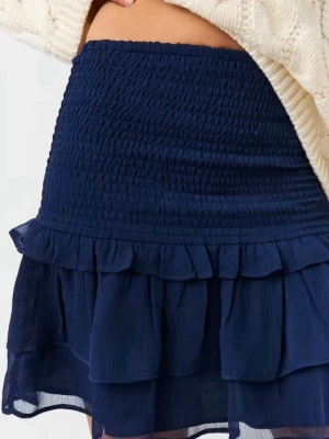 Mörkblå volangkjol  - Supersöt mörkblå kortkjol med dubbla volanglager. Kjolen är gjord i ett lätt och luftigt material som ger en flowy känsla. Perfekt att styla med en stickad tröja eller crop top för en trendig look.