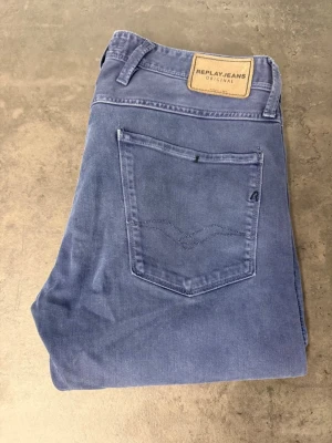 Blå slim fit jeans från Replay 33/34 - Snygga blå slim fit jeans från Replay med klassisk femficksmodell och läderpatch bak i midjan. Jeansen har raka ben och diskreta sömmar på bakfickan. Perfekta för dig som gillar en stilren och modern look.