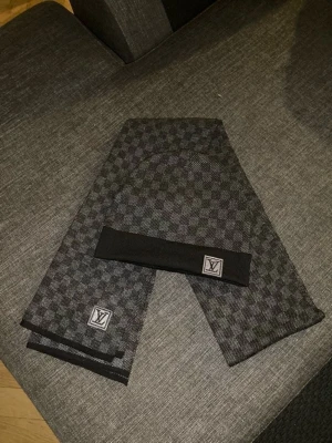 Louis Vuitton halsduk och mössa i kashmir - Snygg halsduk från Louis Vuitton i svart och grått med klassiskt rutmönster och diskret LV-logga. Tillverkad i 100% kashmir för en lyxig och mjuk känsla. Perfekt accessoar för dig som vill ha något exklusivt och stilrent.