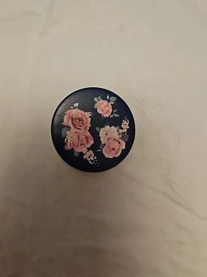Blommig PopSocket mobilhållare - PopSocket mobilhållare med mörkblå bakgrund och rosa blommor på ovansidan. Rund formad och tillverkad i plast. Perfekt för att få bättre grepp om mobilen eller använda som ställ. Passar de flesta smartphones. Har aldrig använts och är helt ny. Lappen är lite dammig i kanterna p.g.a att den har legat i en låda