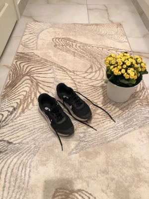 Svarta Nike sneakers med vit sula - Snygga svarta Nike sneakers med vit sula och klassisk vit swoosh på sidan. Skorna har låga skaft och svarta skosnören. Ovandelen är i mesh och syntetmaterial för bra andningsförmåga och komfort. Perfekta för en sportig och avslappnad stil.