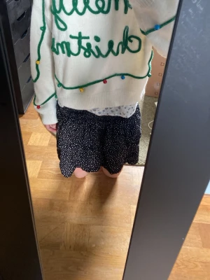 Vit jultröja med text och dekorationer - Vit stickad jultröja med texten 'merry christmas' i grönt och dekorativa färgglada bollar som liknar julgranskulor. Tröjan har rund halsringning, långa ärmar och ribbade muddar. Perfekt för julens alla tillfällen. Bjällrorna låter när man rör på sig.