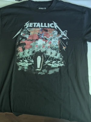 Svart Metallica t-shirt med tryck - Cool svart t-shirt från Metallica med stort färgglatt tryck på framsidan inspirerat av bandets ikoniska album. Klassisk passform med rund hals och korta ärmar. Perfekt för dig som gillar rock och vill sticka ut med en snygg bandtröja.