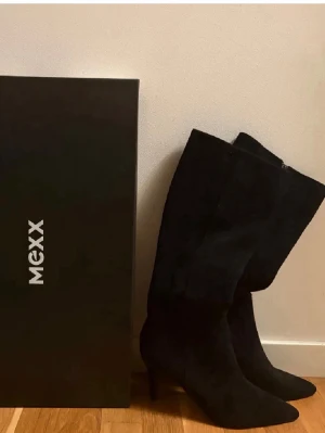 Svarta knähöga stövlar från Mexx - Snygga svarta knähöga stövlar från Mexx med smal klack och spetsig tå. Tillverkade i mockaimitation med dragkedja i sidan, nypris 1330