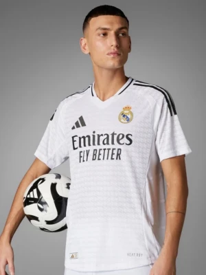 Real Madrid matchtröja Adidas vit - Snygg vit Real Madrid matchtröja från Adidas med svarta detaljer och klubbmärke på bröstet. Tröjan har V-ringning, korta ärmar och tre svarta ränder på axlarna. Tillverkad i lätt och ventilerande material, perfekt för fotbollsträning eller match.