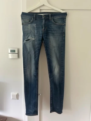 Tiger of Sweden jeans, Style Evolve. - Snygga mörkblå jeans från tiger of Sweden med slimfit passform och slitningar på vänster lår. Klassisk femficksmodell, med bruna sömmar och läderpatch bak i midjan. Jeansen har en tvättad look och är tillverkade i jeansmaterial med dragkedja och knapp. Kontakta vid eventuella frågor!😁