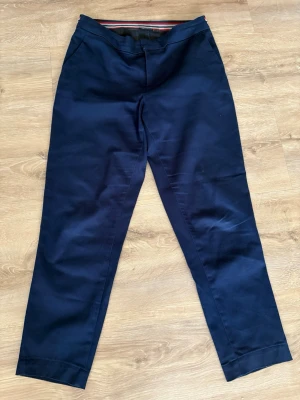 Mörkblå kostymbyxor med randig linning - Snygga mörkblå kostymbyxor med rak passform och diskreta fickor både fram och bak. Linningen har en cool detalj med röd, vit och blå rand. Perfekta för en clean och stilren look. Materialet känns mjukt och har en lätt stretch för extra komfort. Kolla gärna mina andra annonser❗️