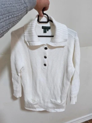 Ralph Lauren Vit Tröja Petite Storlek M Lauren Jeans Co - Säljer en klassisk och fräsch vit tröja från Lauren Jeans Company (Ralph Lauren). Modellen är Petite i storlek M och har en tidlös design med tre eleganta knappar vid bröstet. Tröjan är i mycket fint skick och är tillverkad i en skön kvalitet som passar perfekt till både jeans och mer klädda byxor. Ett högkvalitativt basplagg som lyfter varje outfit! Axlar: 38 cm. Längd (fram, från översta knappen): 53 cm. Längd (bak, från ryggen): 63 cm.