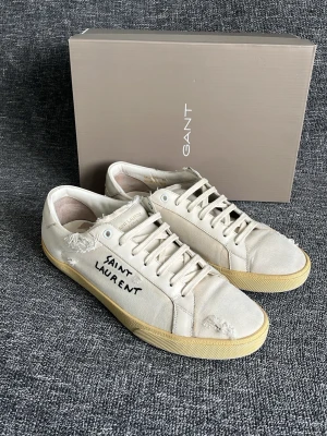 Saint Laurent skor - Hej! Fräscha vit/krämvita Saint Laurent skor i mycket bra skick med tillgjorda slitningar som design! Skorna är som nya och har inga defekter invändigt och utvändigt! Extrabox medföljer. Otroligt sköna och passar perfekt nu denna säsongen och framöver! Har ett nyvärde av 8000kr+ och säljs inte längre vilket gör dessa extra eftertraktade! Storlek 44 och har innermått på 28cm. Skorna är garanterat äkta vilket jag står för. Varmt välkommen att höra av dig 😊mvh DS