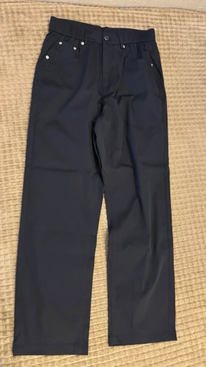 Svarta chinos med raka ben  - Snygga svarta chinos med raka ben och klassisk passform. Byxorna har framfickor med nitar, bälteshällor och två bakfickor. Perfekta för en clean och stilren look. Materialet ser ut att vara bomull eller en bomullsblandning.
