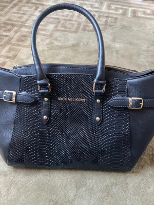 Michael Kors väska - En Svart Michael Kors väska med tre stora fack och tre mindre fack. Jättesnygg, elegant att bära! Även enkel att packa saker i eftersom man lätt kan organisera sina saker! Finns dock lite småskador på väskan men ingenting som syns alls! Kontakta för frågor! 
