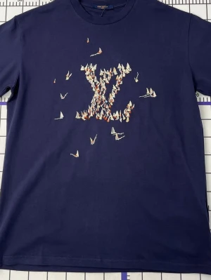 Mörkblå L t-shirt - Mörkblå t-shirt från L med broderat L-motiv på bröstet, där mönstret består av små segelbåtar i vitt, rött och blått. Klassisk rund hals och korta ärmar. Perfekt för dig som gillar exklusiva detaljer och unik design.
