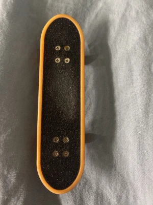 Fingerboard med röd undersida - Fingerboard med svart grepptejp på ovansidan och röd undersida med vitt mönster. Brädan har gula kanter och röda hjul. Perfekt för tricks och skate-entusiaster som gillar miniatyrskateboards.det är nagellack på baksidan som går bort enkelt med nagelborttagning